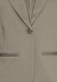 Beiger Blazer aus strukturiertem Stoff, mit Ein-Knopf-Verschluss und zwei Fronttaschen mit kontrastfarbener Einfassung. Schlichte Kerbkragen und klare Linien.