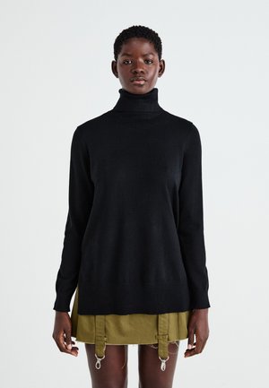 Suéter negro de cuello alto con un cuello acanalado y mangas largas, hecho de una tela suave. Llevado sobre una falda verde oliva con detalles de metal.