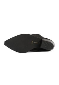 Sole de pantof din suede negru cu o formă ascuțită. Prezintă un grip din cauciuc texturat și detalii subtil embossate aproape de călcâi.