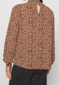Långärmad blus i ett brunt tyg med ett leopardtryck, med en nyckelhålskärning i ryggen och gathered manschetter.