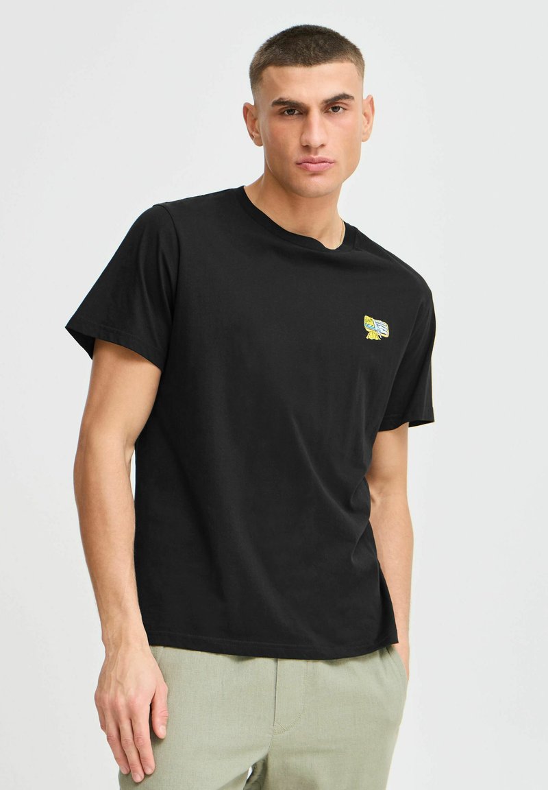 Zwarte katoenen T-shirt met een ronde hals en korte mouwen. Bevat een klein, kleurrijk geborduurd ontwerp op de linkerkant van de borst.