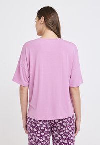 Camiseta de manga corta, holgada, en tejido rosa claro, con escote redondo, mostrando la vista trasera sobre un fondo liso.