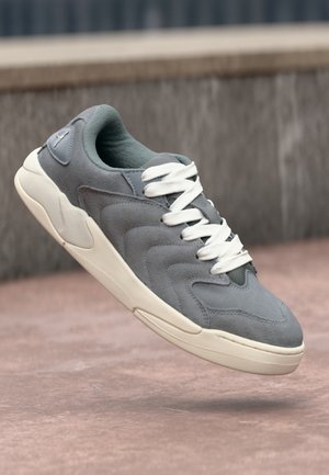 Šedé semišové tenisky s bílými tkaničkami, s texturovaným designem a zaoblenou špičkou. Světle zbarvená podrážka s jemnými akcenty.