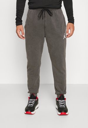 Pantalones de chándal grises con cintura ajustable con cordón, llevan un logo blanco en el muslo izquierdo y puños elásticos. Combínalos con zapatillas negras y rojas.