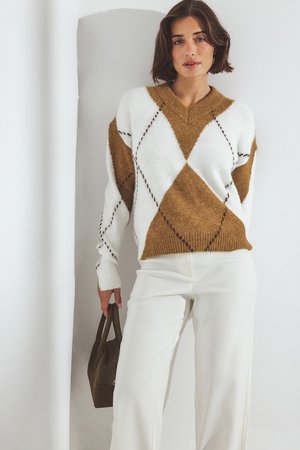 Bruin en wit geblokt patroon sweater met V-hals en ribgebreide manchetten, gecombineerd met witte wijde broek en een kleine donkere tas.