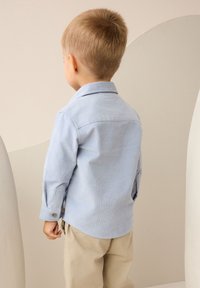 Hellblaues, langärmliges Hemd mit Knöpfen, strukturiertem Stoff, abgerundetem Saum und geknöpften Manschetten, getragen zu beigen Hosen.