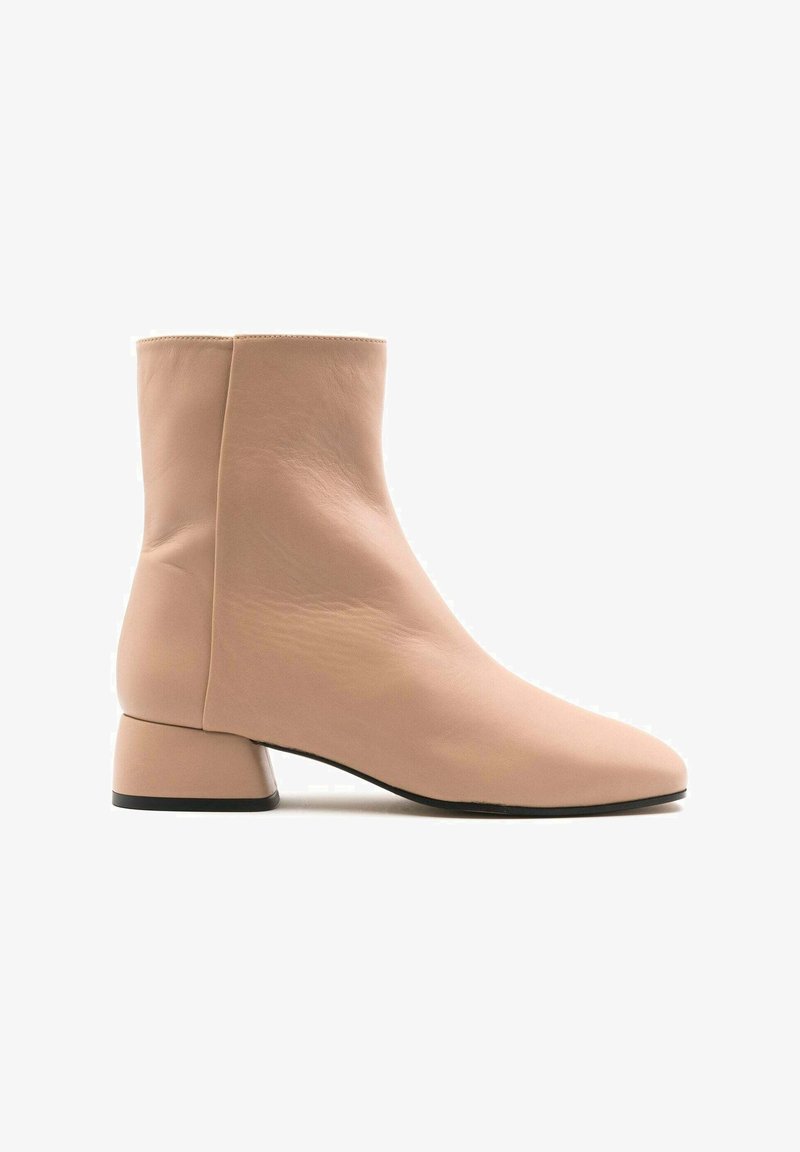 Botas de tobillo rosa claro hechas de cuero suave, con un tacón cubano cuadrado y una punta afilada, con costuras mínimas y un diseño elegante.