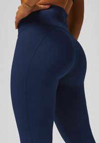 Marineblaue high-waist Leggings mit schmalem Schnitt, ausgestattet mit flachen Nähten und glatter Textur, die die konturierte Rückseite betonen.