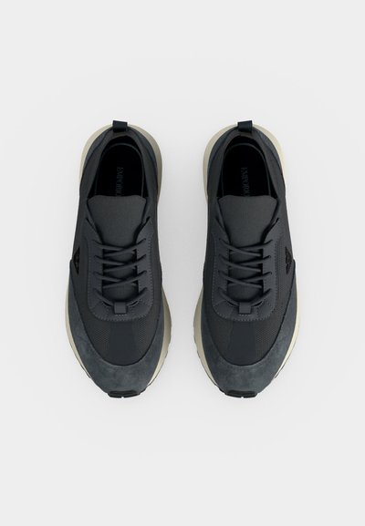 Paire de baskets décontractées gris foncé avec des lacets noirs et des semelles claires, vues de dessus sur un fond clair.