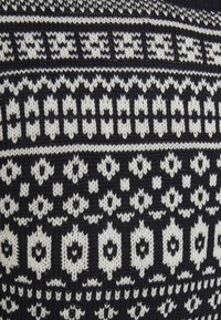 Pull en tricot présentant un motif géométrique bleu et blanc, avec des formes et des textures alternées dans un matériau semblable à de la laine.