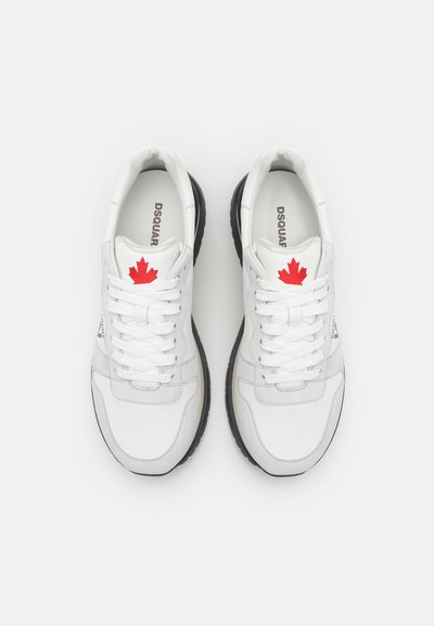 Hvite lær sneakers med svarte gummisåler, med en rød lønnsløvlogo på tungen og sømdetaljer på overdelen.