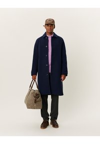 Ναυτικό μαλλί παλτό με κουμπί κλείσιμο, μοβ πλεκτό πουλόβερ, γκρι παντελόνι, καφέ δερμάτινα παπούτσια και τσάντα σε καρό σχέδιο με καφέ λεπτομέρειες.