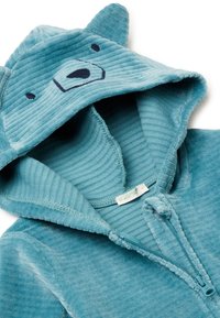 Tuta con cappuccio in morbido tessuto color teal con design di un volto d'orso. Include una chiusura con zip frontalmente e dettagli testurizzati su cappuccio e maniche.
