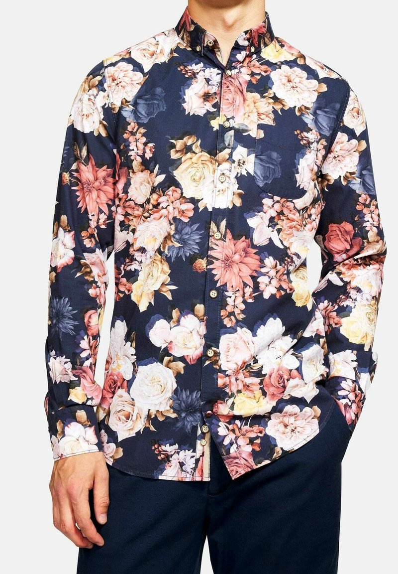 Camicia blu navy con motivo floreale che presenta un mix di fiori rosa, bianchi e blu, colletto con bottoni, maniche lunghe e dettaglio con taschino sul petto.