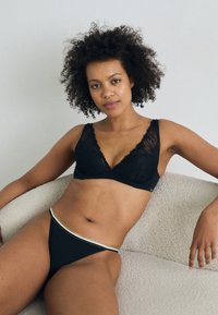 Svart triangulär bralette med spetskant och svart trosa med en metallisk rand. Mjuk tyg med en jämn textur, åtsittande design.