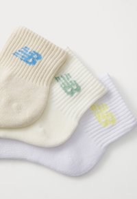 Tre par med korte sokker: beige, hvite og lys grønne. Hver av dem har ribbet tekstur og en liten logo i blå, grønn og gul.