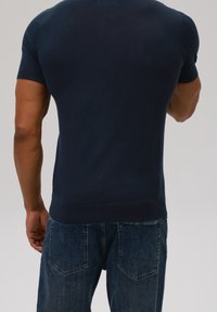 Marinblå kortärmad stickad tröja med ribbade axlar och en figurnära passform, i kombination med ljusblå denimjeans med bakfickor.