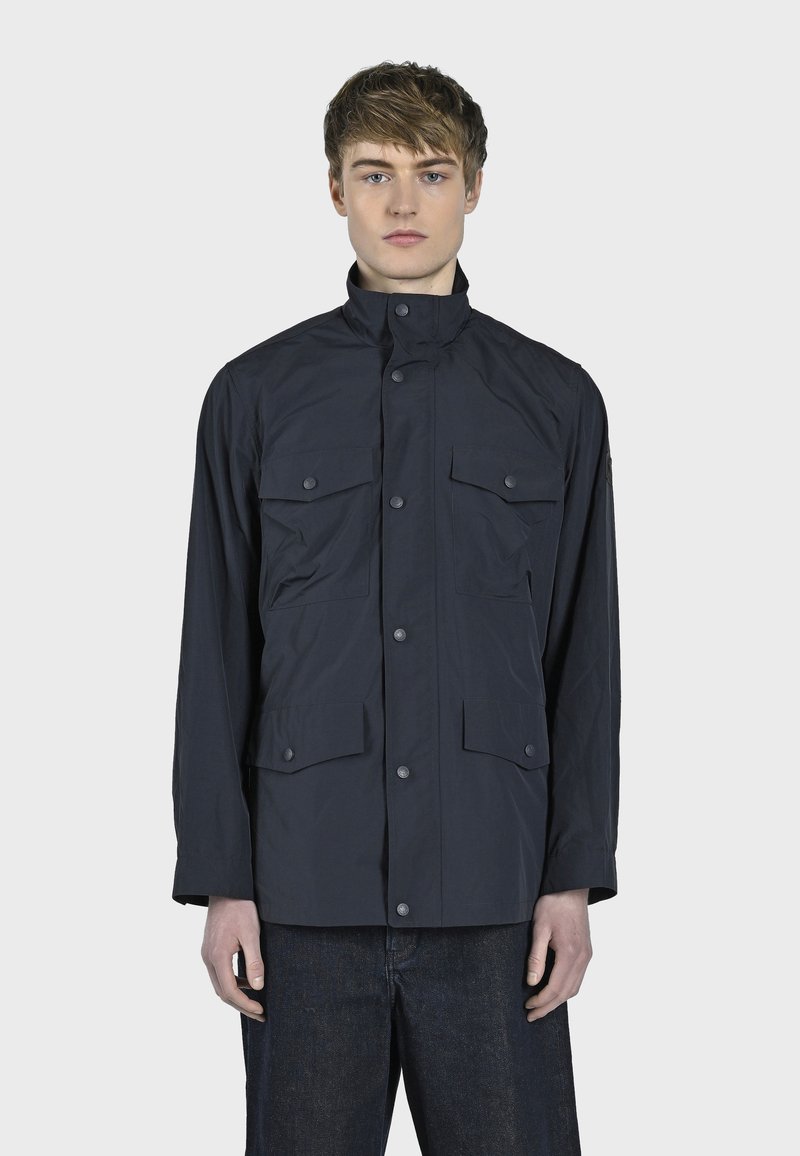 Námořnický modrý, lehký kabát s vysokým límcem, zapínáním na knoflíky a čtyřmi předními kapsami. Hladká textura, minimalistický design a dlouhé rukávy.