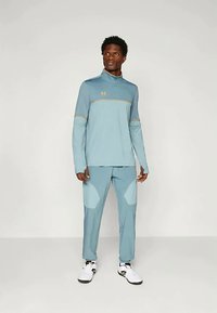 Top de sport lungă, de culoare albastru deschis, cu accente aurii și pantaloni asortați tapered, având panouri texturate la genunchi și o țesătură ușoară.