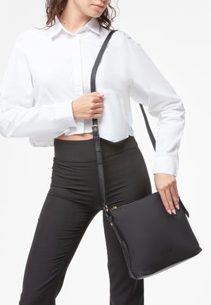 Borsa a tracolla nera realizzata in materiale liscio, dotata di chiusura con zip, cinturino regolabile e design minimalista senza loghi visibili.