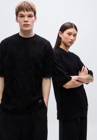 Μαύρα πλεκτά πουλόβερ με υφασμένους μοτίβους, στρογγυλές λαιμόκοψεις και κοντά μανίκια. Φορεμένα με φαρδιά μαύρα παντελόνια.