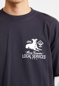 Schwarz Baumwoll-T-Shirt mit weißem grafischen Text und einer Hundillustration. Rundhalsausschnitt mit kurzen Ärmeln. Bequeme Passform.