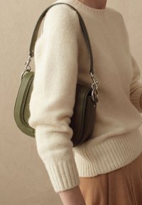 Borsa a tracolla in pelle verde con una forma strutturata, caratterizzata da hardware in argento e una tracolla rimovibile, abbinata a un maglione lavorato a maglia color crema.