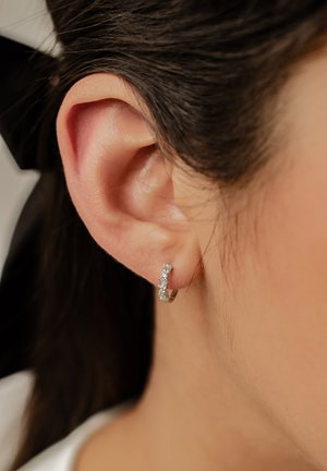 Silberne Creolen mit rechteckigem Design, die klare Edelsteine in einem linearen Muster zeigen. Nahaufnahme des Ohres und des Ohrrings.