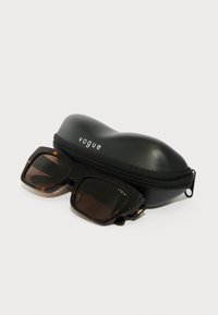 Ochelari de soare rectangulari negri cu lentile maro, așezați pe un toc dur negru cu fermoar, având brandingul alb "vogue".