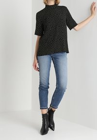 Svart blus med prickar, hög halsringning och korta ärmar, matchad med ljusblå jeans och svarta klackstövlar.