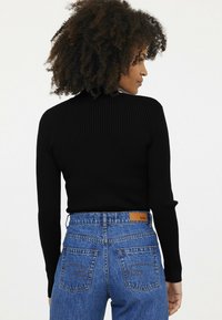 Schwarzes, geripptes Langarmshirt mit hohem Kragen, kombiniert mit hochgeschnittenen blauen Denim-Jeans mit einem Lederetikett und kontrastierenden Nähten.