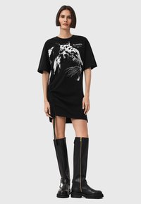 Abito t-shirt nero con grafica di tigre bianca, dettaglio di arricciatura laterale e vestibilità rilassata, abbinato a stivali alti neri con zip.
