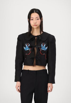 Black cropped jacket with a large collar, three front bows, and colorful embroidered bird designs on chest. Smooth fabric texture.