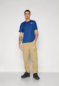 Camiseta azul de manga curta com padrão texturizado, calças castanho claro com bolsos com fecho, e ténis pretos desportivos. Logótipo The North Face na camisola e nas calças.