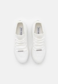 White athletic shoes with a textured knit upper, flat laces, and a metallic accent on the tongue. No visible logos or patterns.