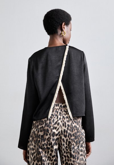 Black textured top with a back slit trimmed in cream, paired with loose leopard-print pants featuring a drawstring waist.