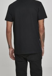 Zwart T-shirt met korte mouwen en rechte snit, gemaakt van katoen. Heeft minimale stiksels en een effen achterkant. Draagt zwarte broek.