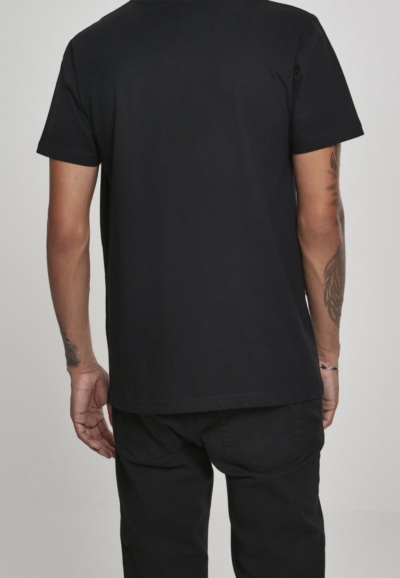 Zwart T-shirt met korte mouwen en rechte snit, gemaakt van katoen. Heeft minimale stiksels en een effen achterkant. Draagt zwarte broek.