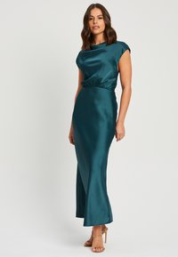 Svetlozeleni satenski obleki s prilegajočim pasom, kratkimi rokavi in dolgim A-linijskim krilom. Gladka tekstura s subtilnim sijajem.