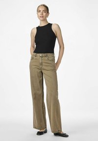 Top sin mangas negro combinado con jeans beiges de pierna ancha y tiro alto. El conjunto presenta una silueta curvilínea y detalles de diseño minimalistas.