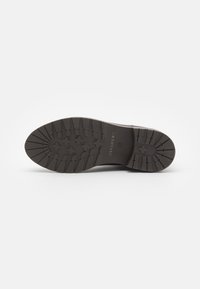 Semelle en caoutchouc marron avec un motif texturé et cannelé et le logo "PAVEMENT" en relief près du talon. Conçu pour l'adhérence et la durabilité.