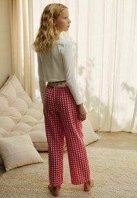 Fehér, rövidre szabott, hosszú ujjú felső és piros kockás, bő zakó nadrág virágmintás derékkal, hátulról nézve.