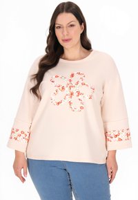 Sweatshirt roz deschis cu un model floral, având o aplicație în formă de floare la centru și accente florale pe manșete.