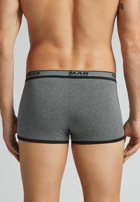 Grijze boxershorts van zacht materiaal, met een zwarte elastische tailleband waarop de merknaam prominent is weergegeven. Glad textuur en slim fit ontwerp.