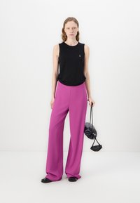 Zwarte mouwloze tanktop; losvallend, gecombineerd met hoge taille, wijde broek in een levendig roze. Klein logo-detail op de top.