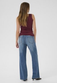 Débardeur bordeaux avec dentelle, associé à un jean en denim large bleu clair. Le modèle est de dos, montrant les poches arrière et la coupe des jeans.