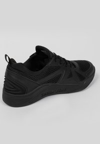 Chaussure de sport noire en combinaison de matériaux en mesh et synthétiques, avec une semelle texturée et des accents de marque.