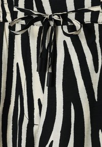 Zebras rakstainas bikses melnā un krēmkrāsā, kas aprīkotas ar elastīgu jostasvītru, auklu ar melniem galiem un mīkstu, fakturētu audumu.