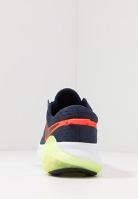 Námořnické běžecké boty s texturovaným vrškem, pomerančovými akcenty a silnou bílou mezipodešví s úsekem z zelené gumy na patě.
