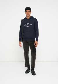 Ναυτικό φούτερ με κουκούλα, μπροστά τσέπη και λογότυπο, σε συνδυασμό με υφασμάτινα σκούρα καφέ καμπάνες από χονδροκομένο πανί και μαύρες μπαλαρίνες. Απλή τσάντα ώμου.